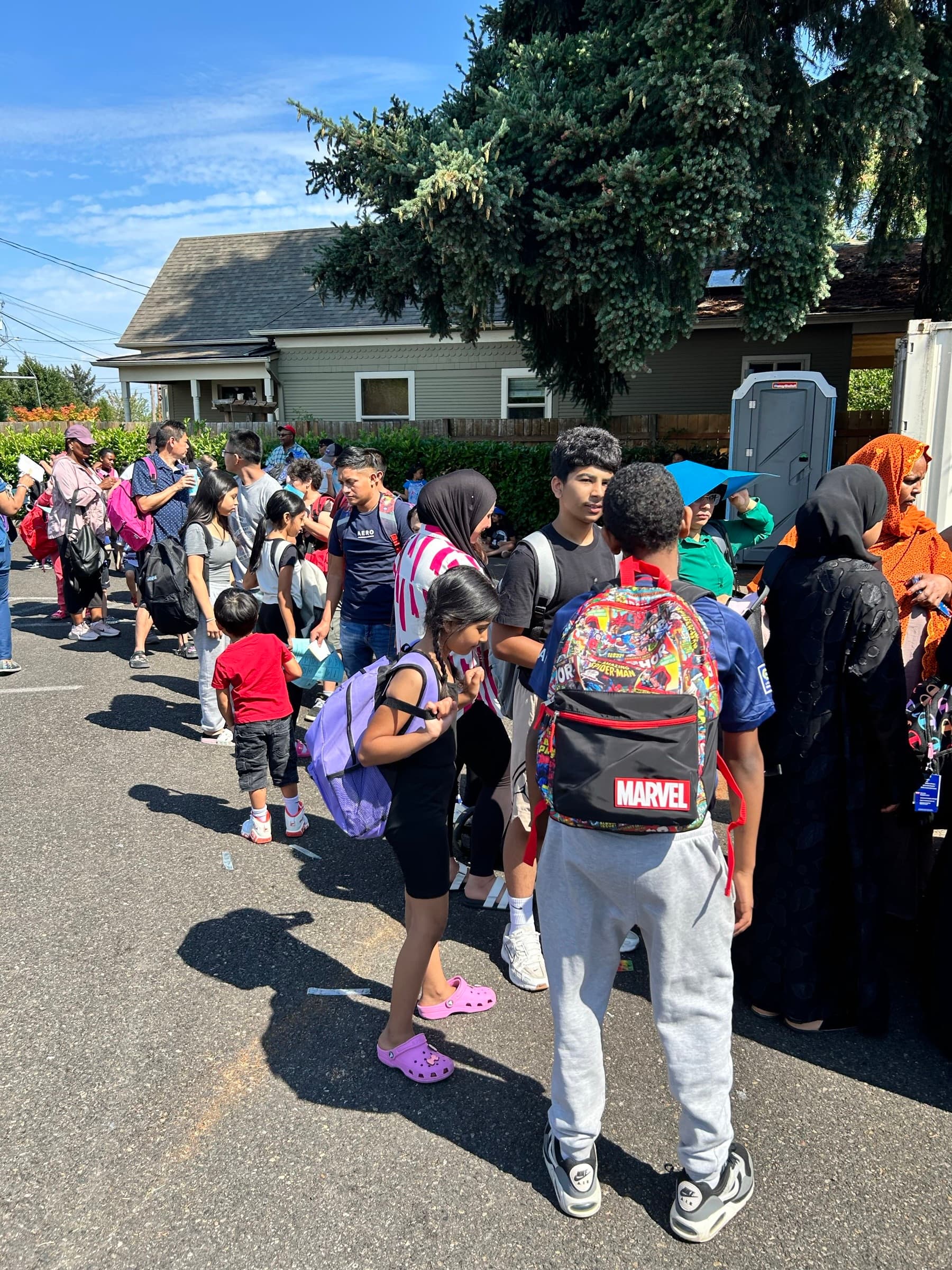 Families lined up outside with backpacks at a community distribution day
