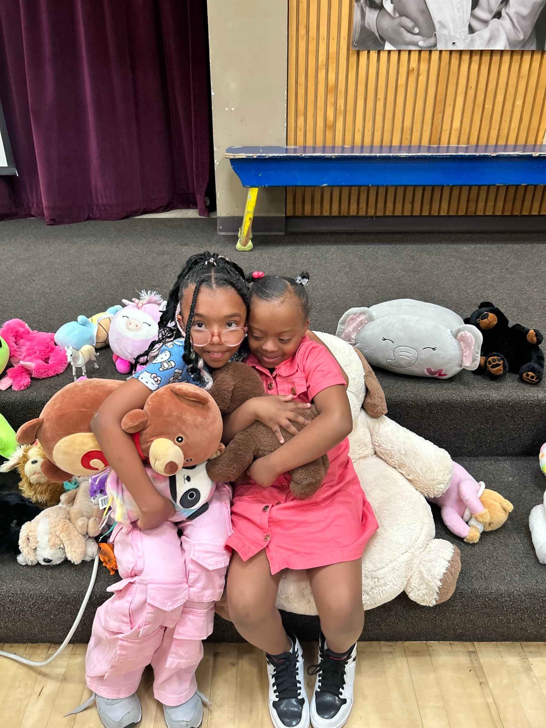 Two girls hugging surrounded by donated stuffed animals