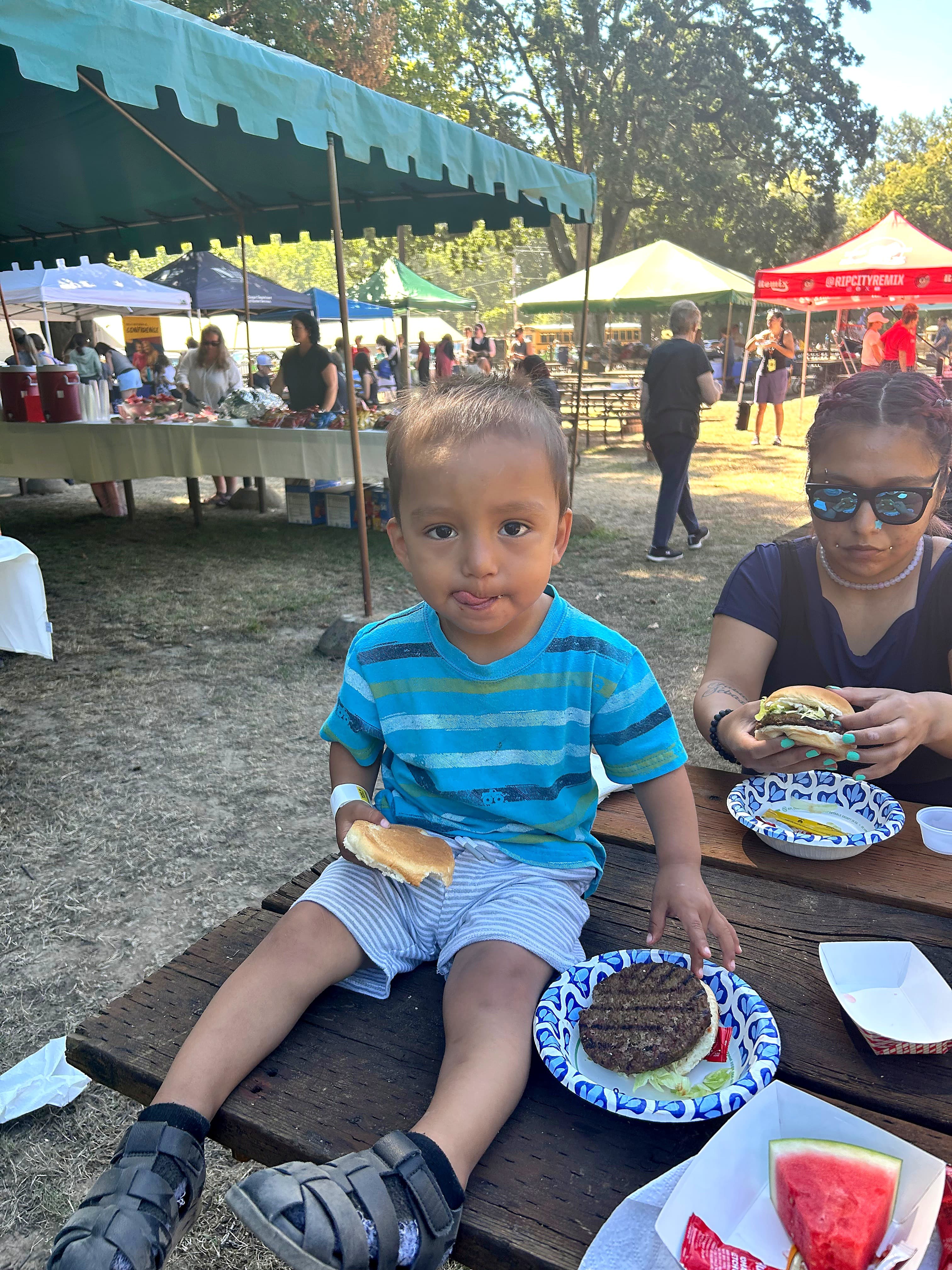 A boy eating a hamburger on a picnic bench at Oaks Park Day