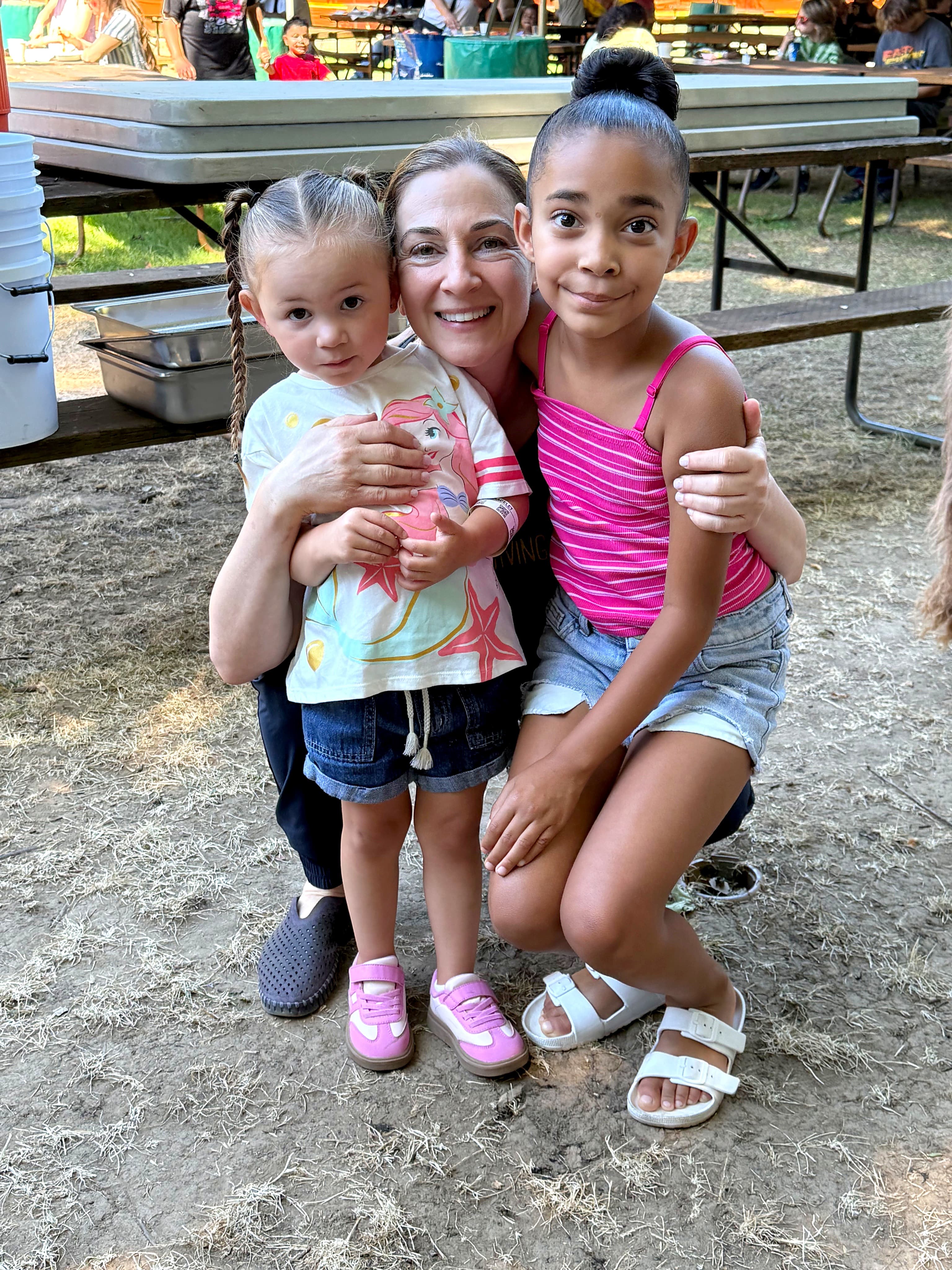 A volunteer hugging two girls at a picnic table at Oaks Park Day