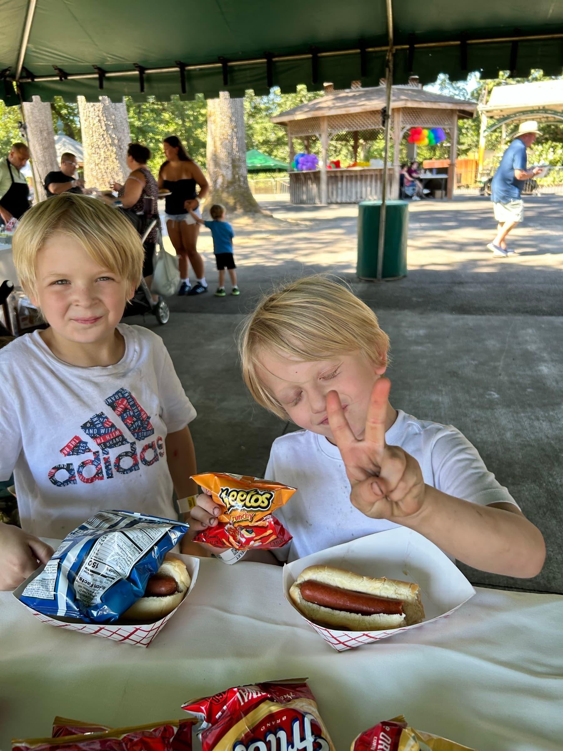 Two kids eating hot dogs and chips under the pavilion at Oaks Park Day