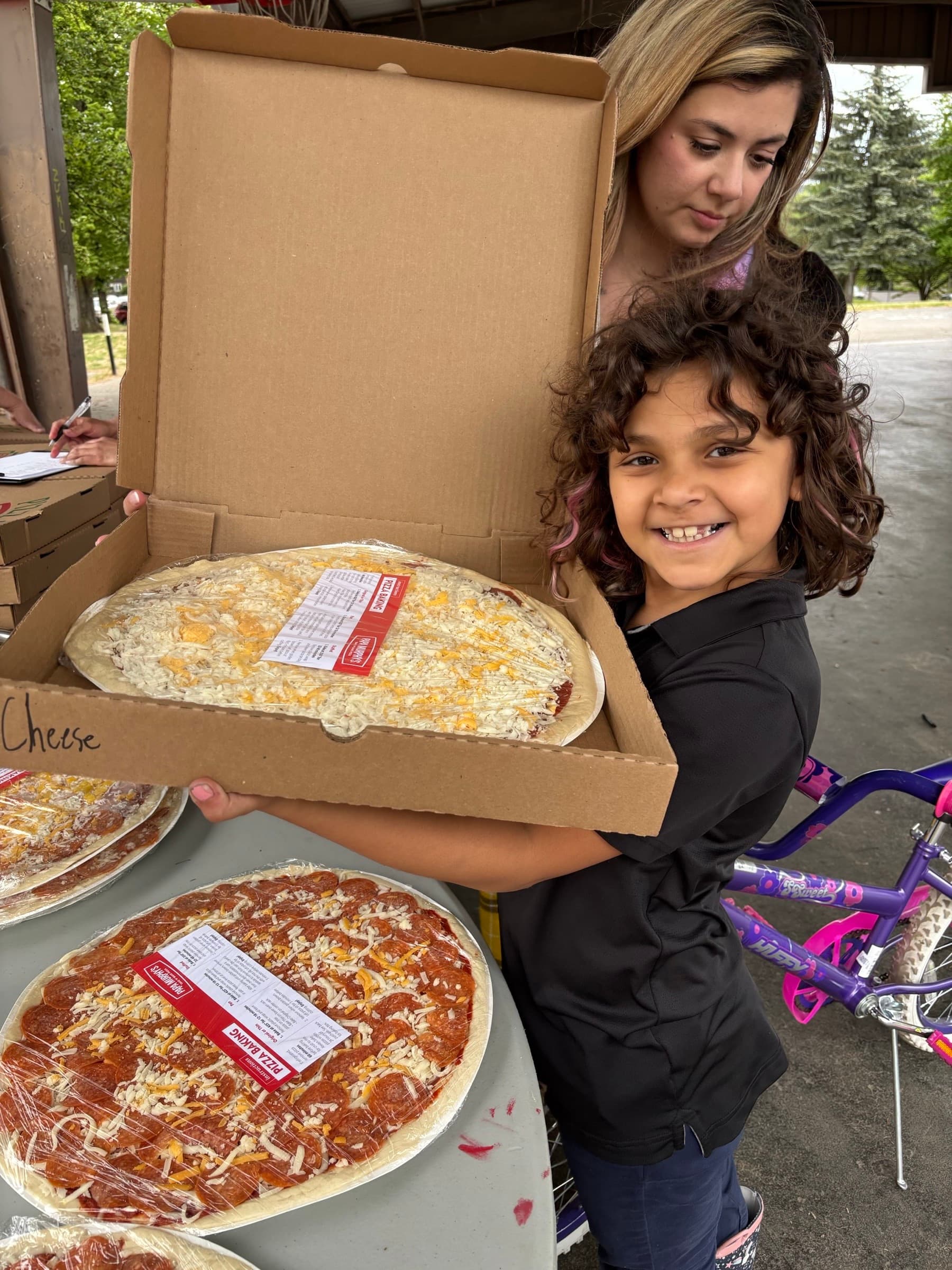 A mother and daughter picking up a fresh cheese pizza at a Papa Murphy's distribution event