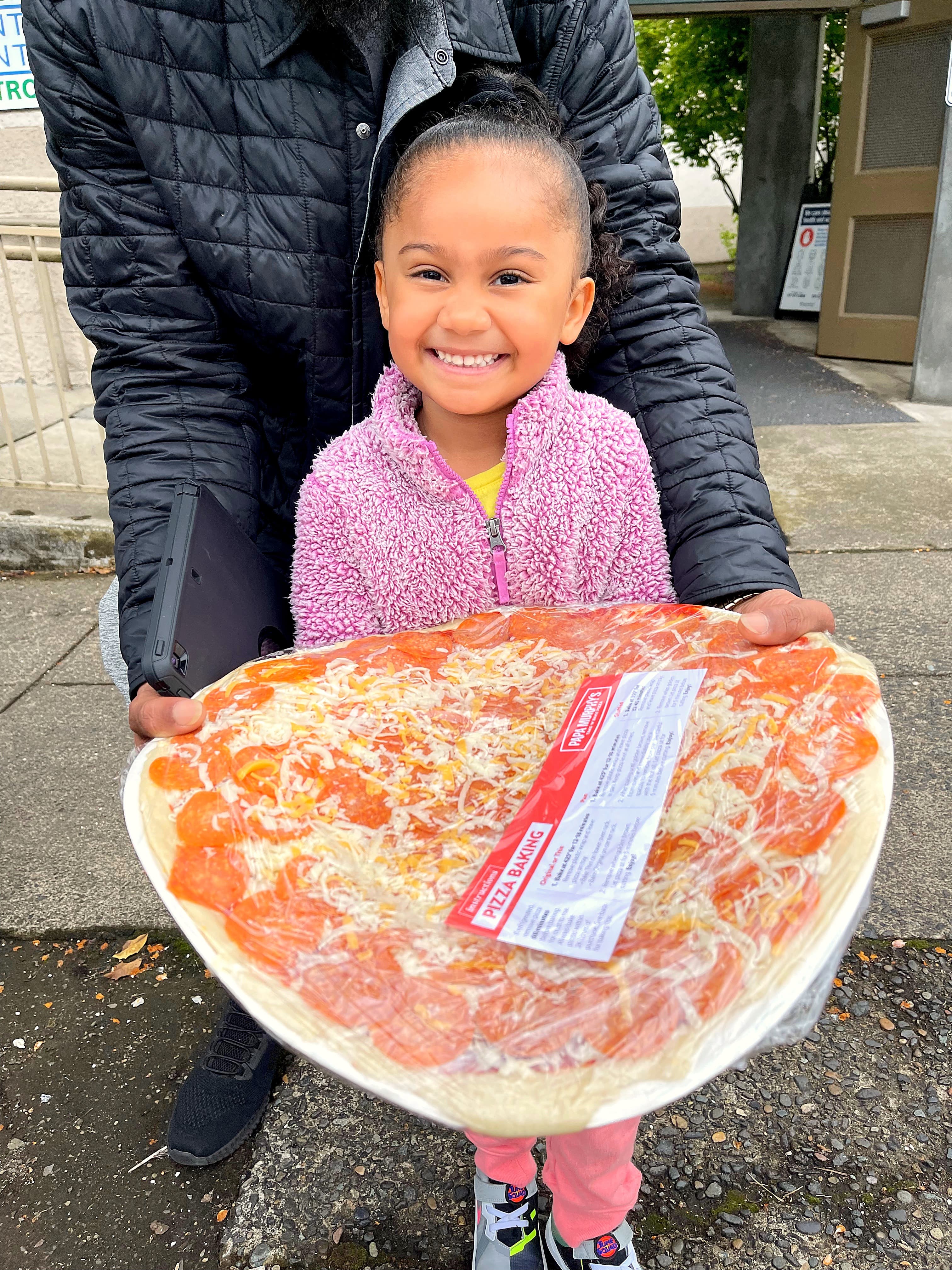 A girl smiling and holding a Papa Murphy's take-and-bake pizza outside a distribution site