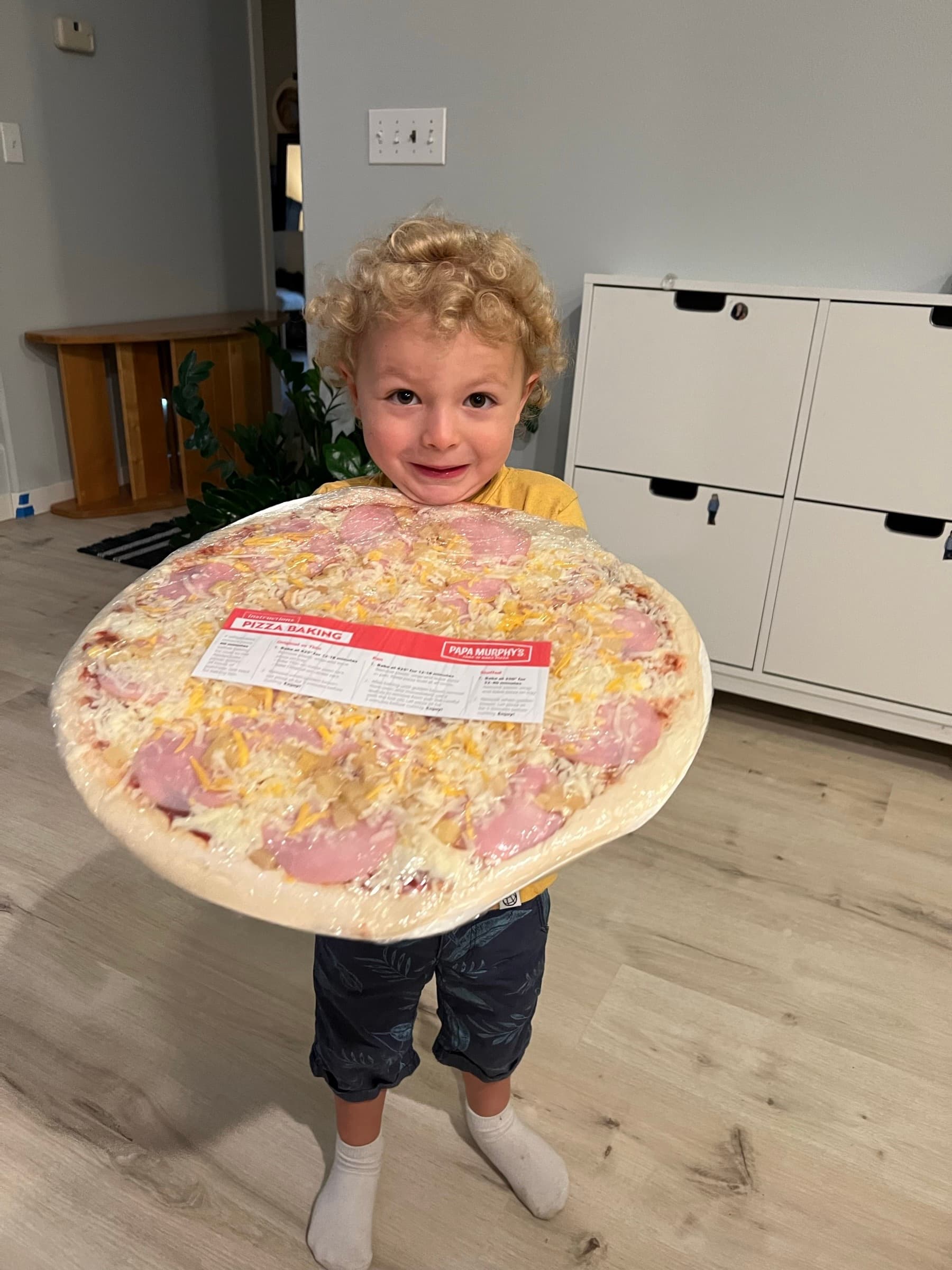 A boy holding a take-and-bake pizza at home